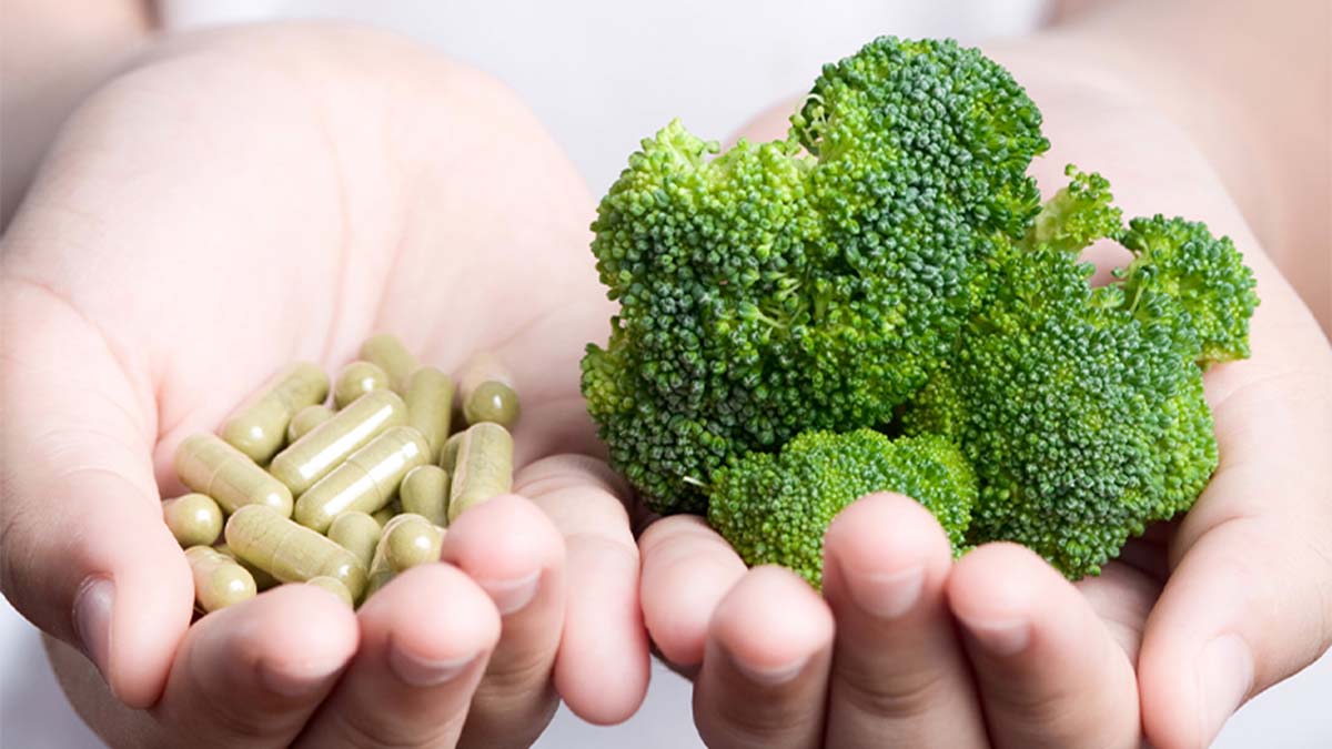 Pessoa a segurar brócolos e cápsulas de suplementos alimentares